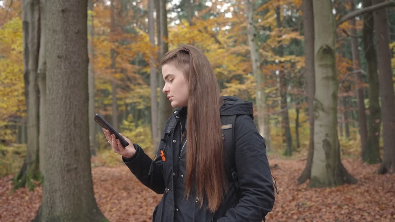Giovane donna in escursione in una foresta autunnale con lo smartphone