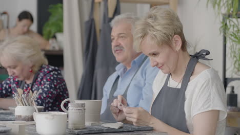 a group of elderly people at a master class in pottery together sculpt and cut a drawing on cups of clay for the manufacture of ceramic dishes