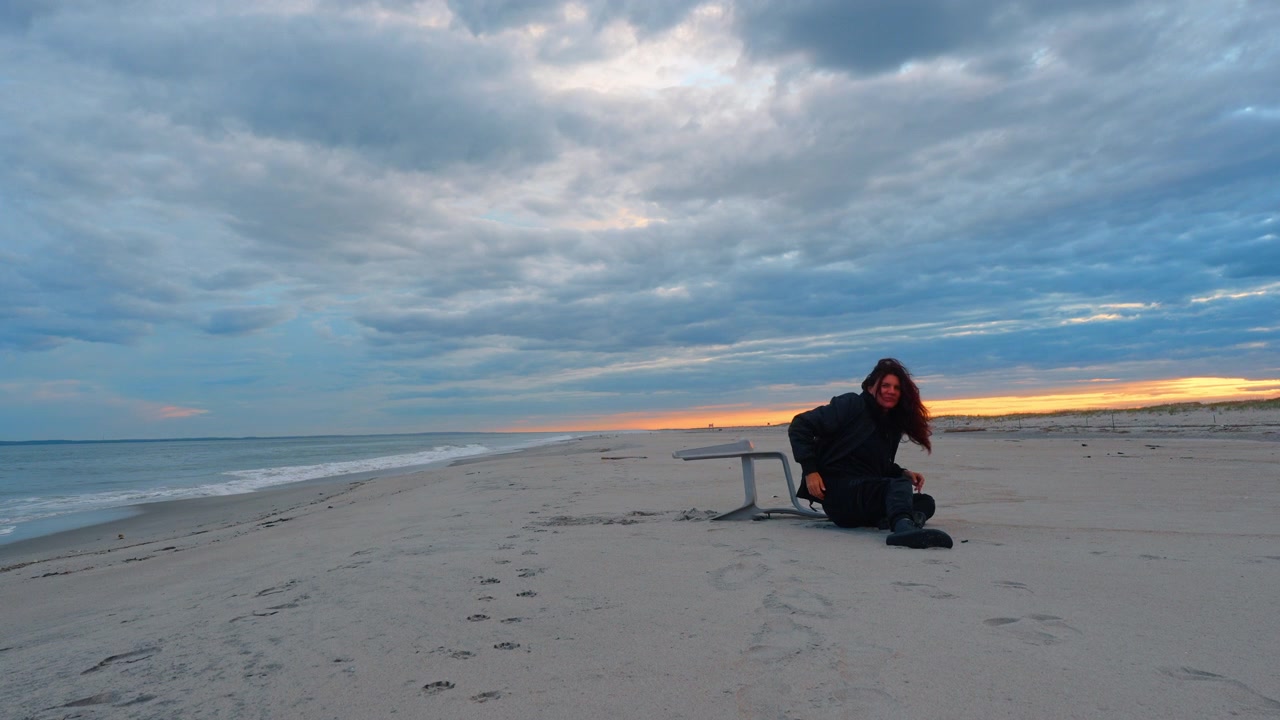 Person lying on a chair with legs in the air on a beach during sunset. A person is lying on a beach chair with their legs in the air.
