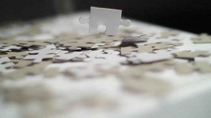Primo piano di pezzi di puzzle bianchi e grigi che cadono al rallentatore su una superficie bianca e rimbalzano, con uno sfondo scuro