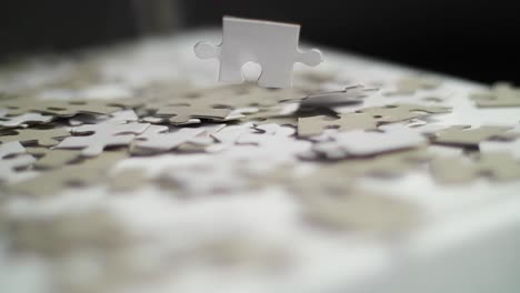 close up of white and gray puzzle pieces falling in slow motion on a white surface and bouncing off with a dark background