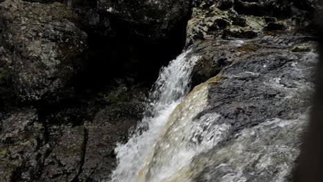 Natural-waterfall-pouring-cold-river-water-rapidly-down-over-brown-mossy-rocks-in-rugged-wilderness-with-bubbles-and-splashing