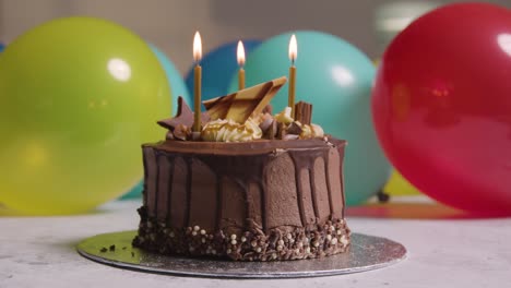 pastel de cumpleaños de chocolate decorado con velas que se apagan en la fiesta con globos en segundo plano