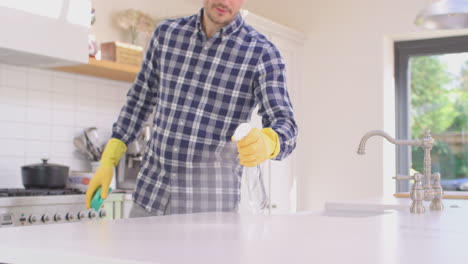 man at home in kitchen wearing rubber gloves cleaning down work surface using cleaning spray - shot in slow motion