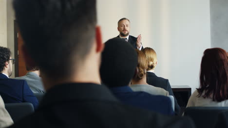 caucasian mature businessman wearing formal clothes speaking at a conference in front of many people