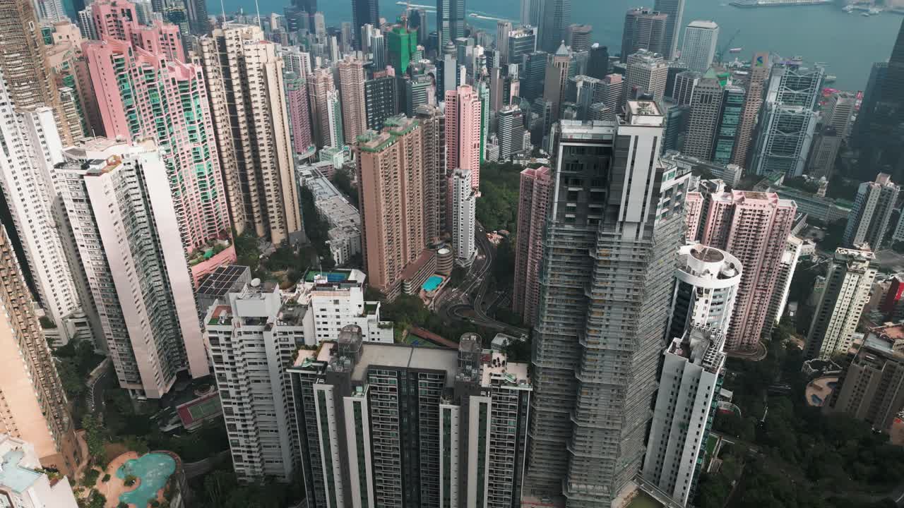 Imagens aéreas panorâmicas de drone do centro de Hong Kong vistas do Pico Victoria num dia ensolarado, mostrando o horizonte, o porto e a densa paisagem urbana.