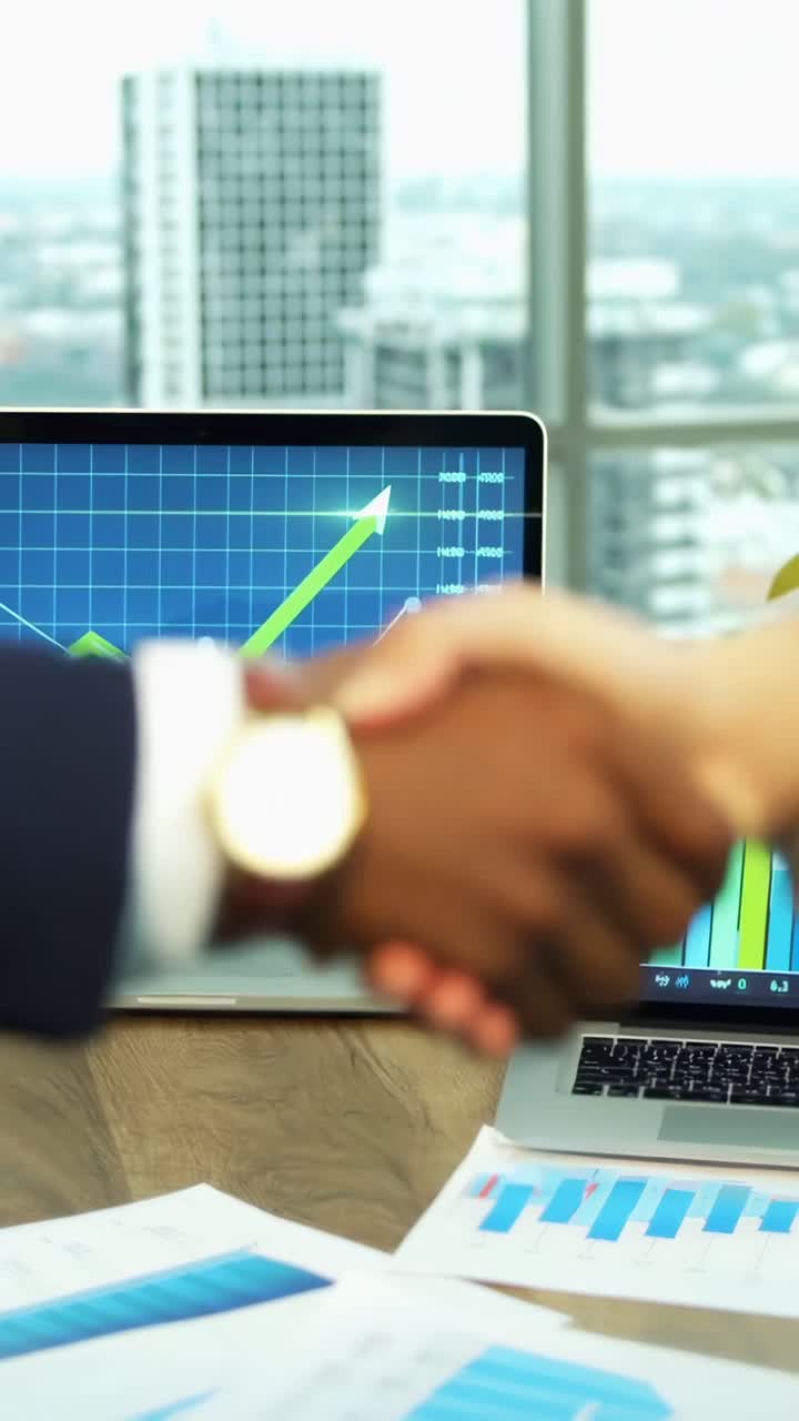 Video en primer plano de un apretón de manos en un entorno de oficina, con ángulo de cámara ascendente y gráficos visibles.