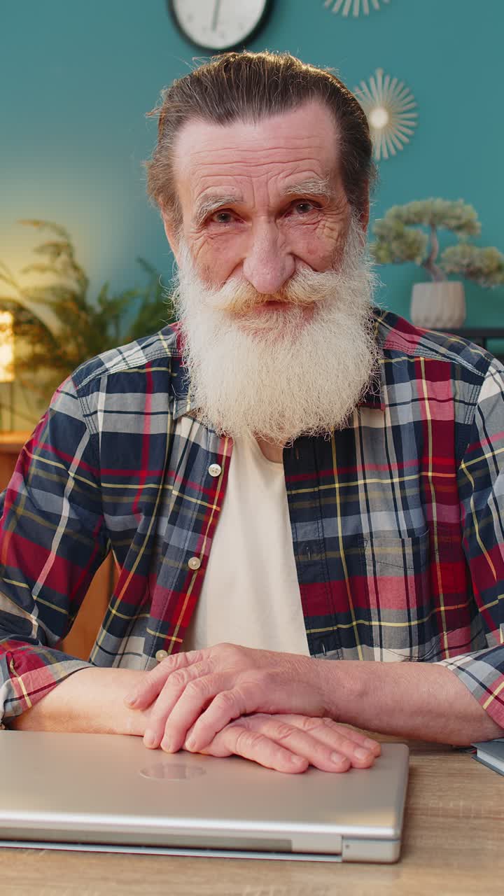 Abuelo feliz cerrando el ordenador portátil después de terminar de trabajar en la mesa de su oficina en casa.