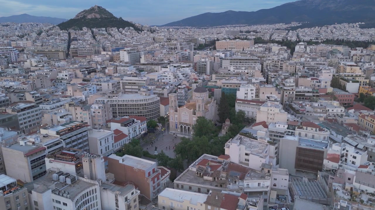 La Cattedrale Metropolitana di Atene si erge tra isolati cittadini densamente popolati mentre un drone orbita nella soffusa luce serale