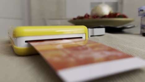 yellow portable photo printer printing an image on a tabletop with soft focus