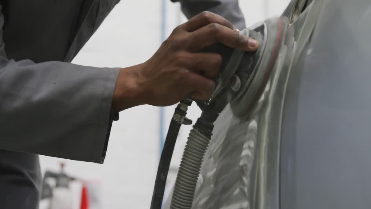 mecánico de automóviles afroamericano que lleva una máscara facial y puliendo un lado de un automóvil con un molinillo