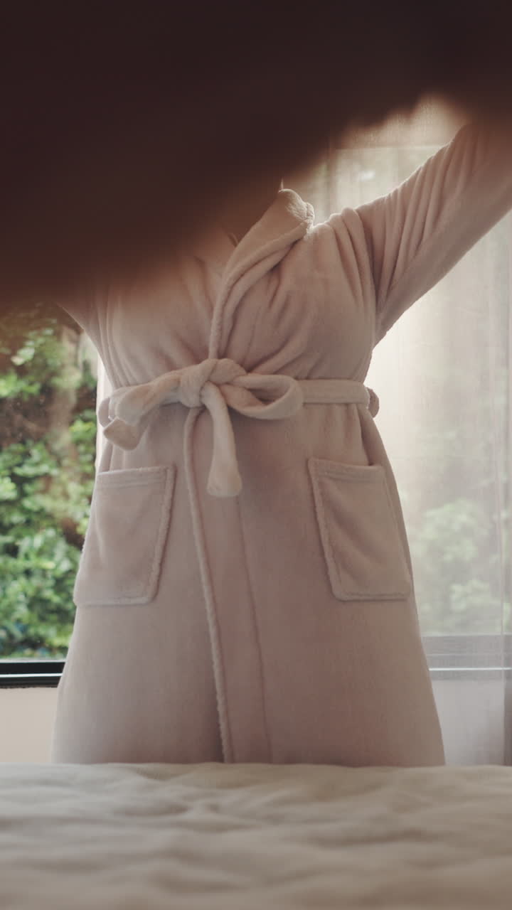 Happy Young Woman Stretching in Bathrobe by Window