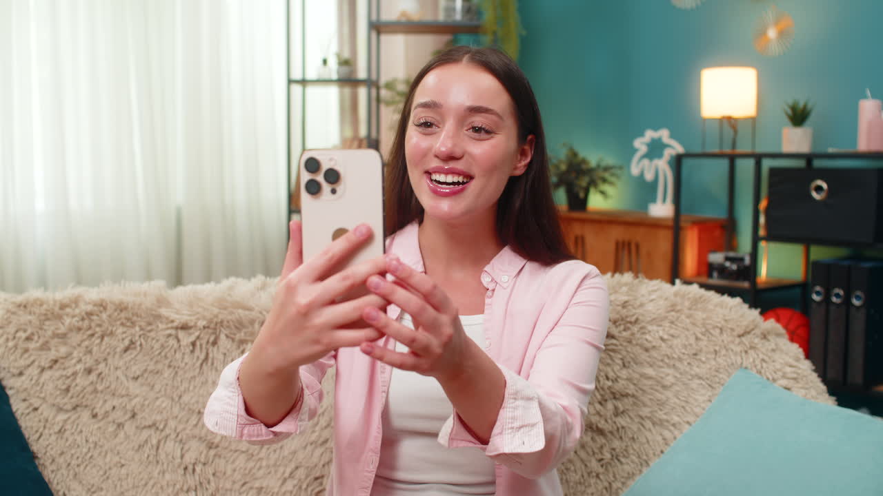 Young woman laughing on smartphone selfie video call waving hands and sharing big smiles with friend