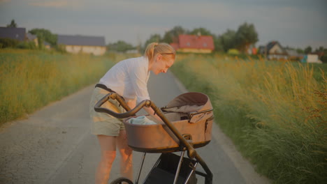 young mother giving pacifier to baby in stroller at sunset