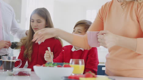 padres ayudando a los niños en uniforme escolar a prepararse mientras comen el desayuno en el mostrador de la cocina