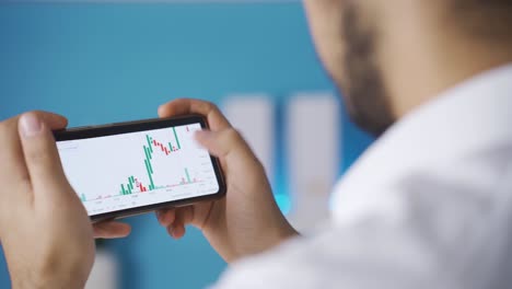 Male-hands-holding-phone-checking-stock-market-chart-for-trading-and-investing-in-crypto-exchange.