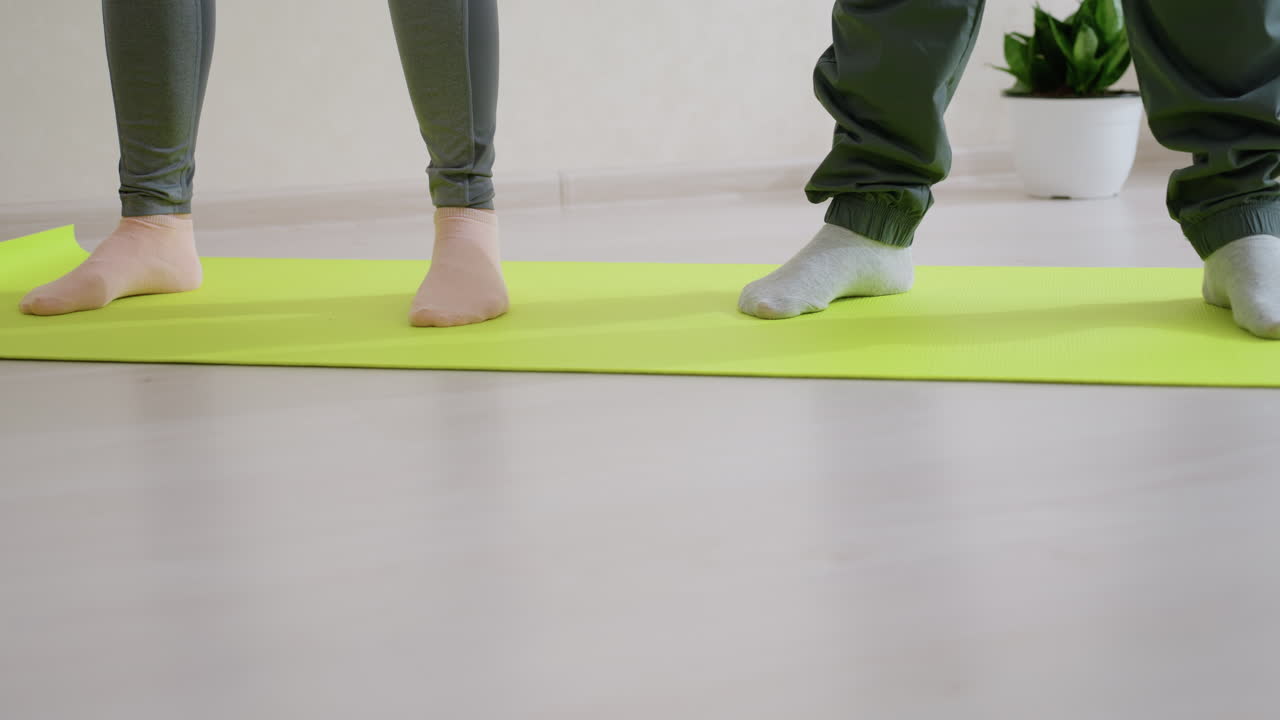 Leg view of people standing on bright green fitness mat indoors during workout, showing lower body in socks, exercise balance and training posture