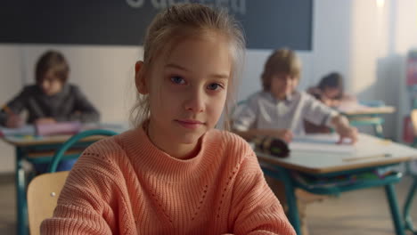 serious student posing at camera in classroom. cheerful girl sitting at desk