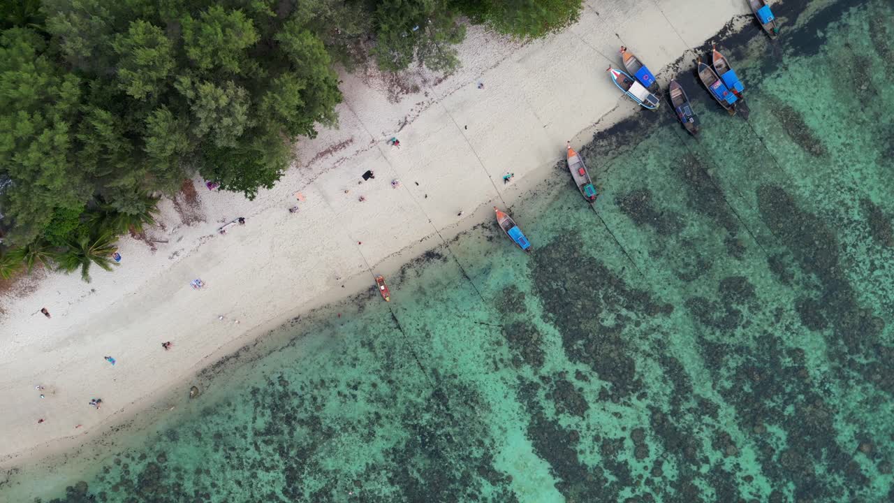 barcos coloridos atracados en una playa de una isla tropical, con turistas caminando por la arena blanca