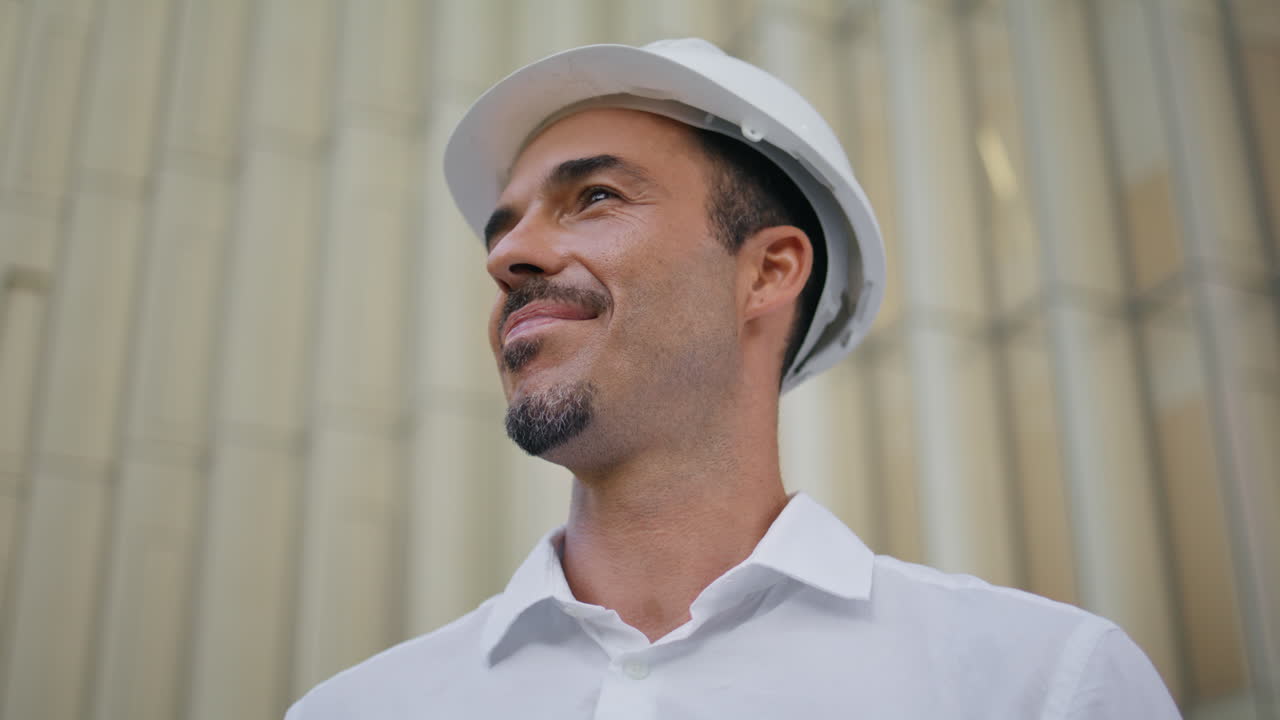 Portrait latin builder smiling camera at architecture background. Man n hardhat