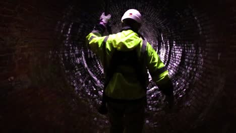 a sewer district worker leads the path with a light down an old 19th-century sewage tunnel