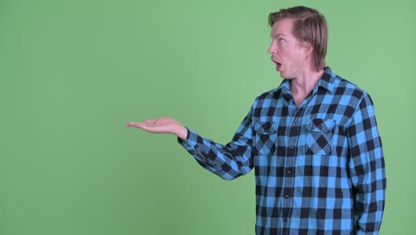 portrait of caucasian man holding something and looking surprised shot against green studio background