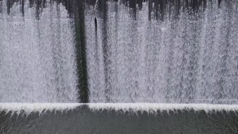 Aerial view of water cascading over a dam, creating a textured, dynamic scene with consistent lighting and smooth camera movement