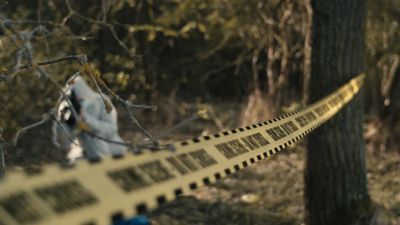 Crime scene investigation outdoor, yellow tape hanging between trees, csi photographer in background