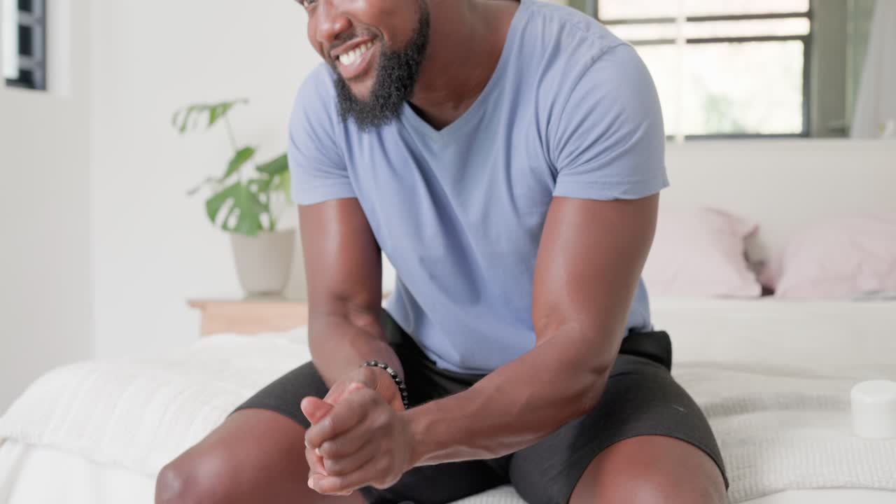 Vertical video: African American man pressing pump, rubbing lotion into hands for moisture on bed