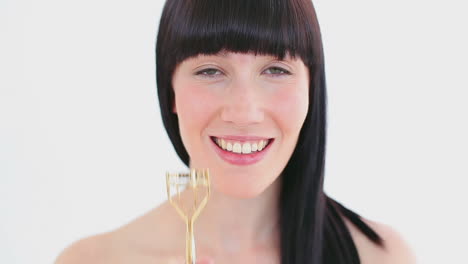 smiling brunette using a curler for her eyelashes