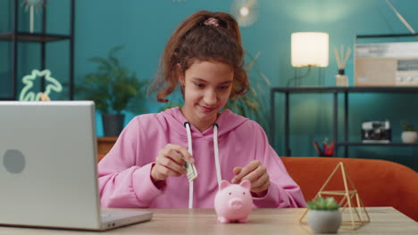 preteen school girl putting one dollar cash money into piggy bank enjoying her first saving earning