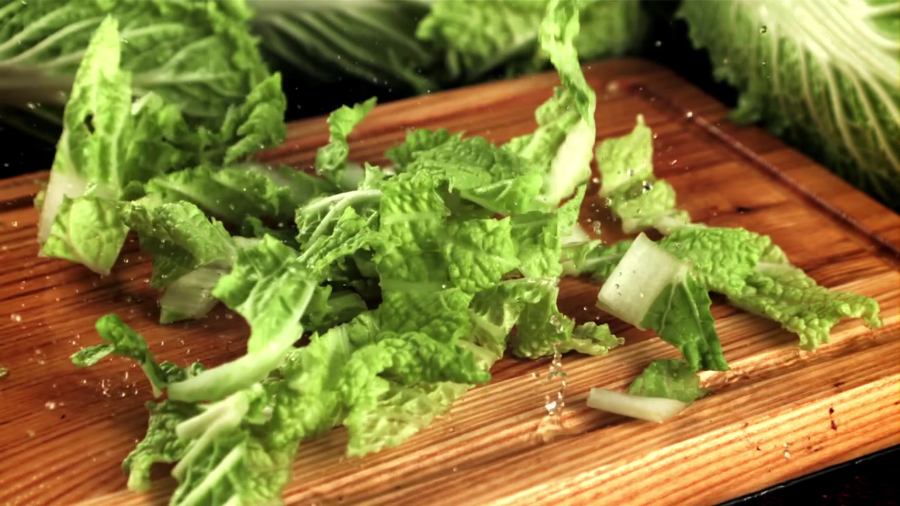 Lechuga verde fresca picada cayendo sobre una tabla de cortar de madera a cámara lenta