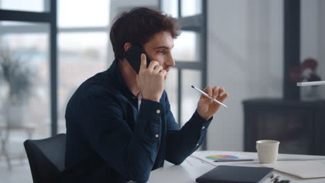 vista de primer plano de un empresario sonriente hablando con su teléfono inteligente en la oficina de su casa