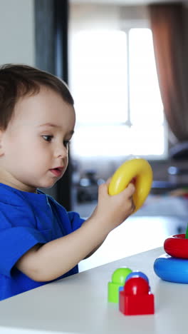 beautiful caucasian toddler sits at the desk. cute child plays with colorful toy pyramid. vertical video