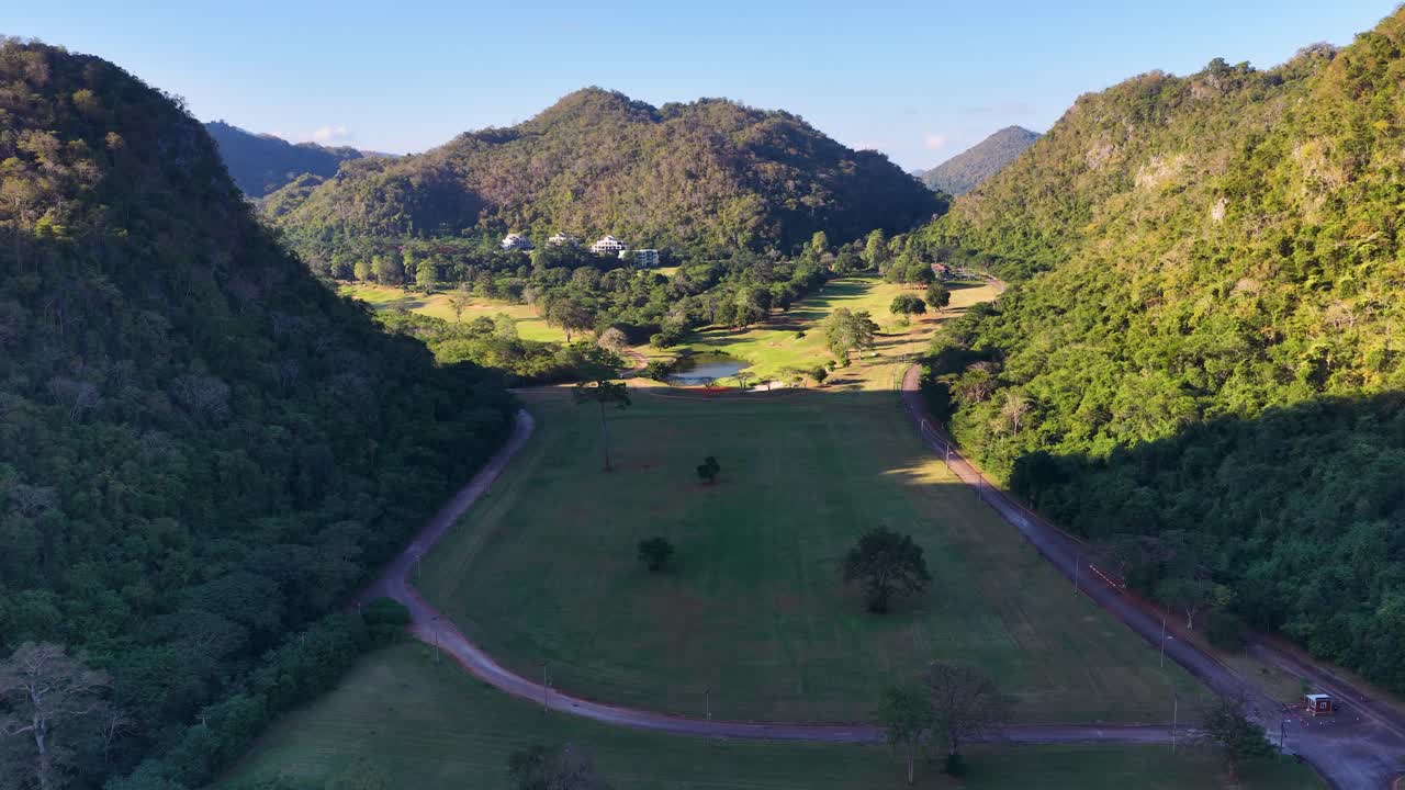 Pengambilan gambar drone dari sudut tinggi memperlihatkan lapangan golf hijau yang dikelilingi oleh pegunungan tropis yang dramatis