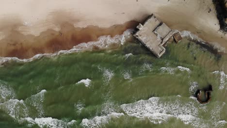 aerial top down view of waves crashing against old german bunkers from world war 2 located on a beach on at the danish west coast