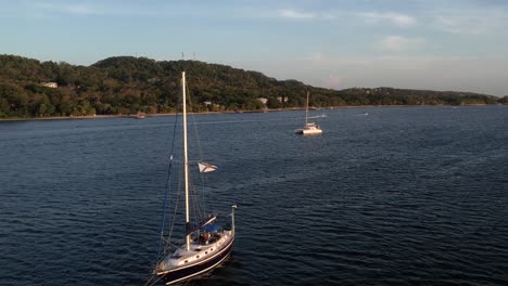 drone flying between sail boats on clear blue sea surface with coral reef and moving towards the land