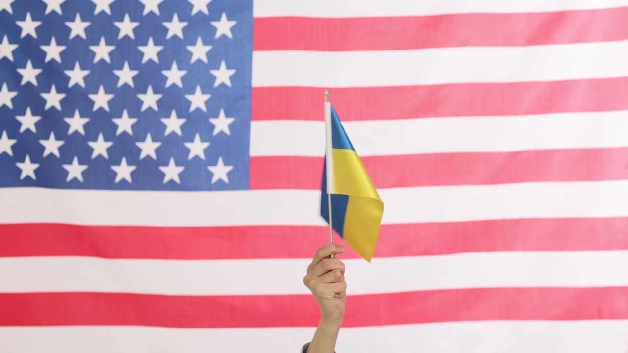Hand holding Ukrainian flag in front of American flag