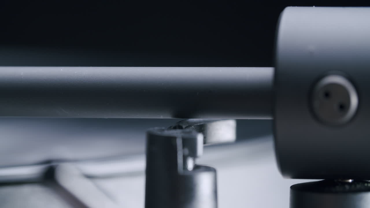 Close up shot of the pick-up of a record player with soft commercial light in a dark studio. The arm gets lowered to play the record. After playing, it goes up again