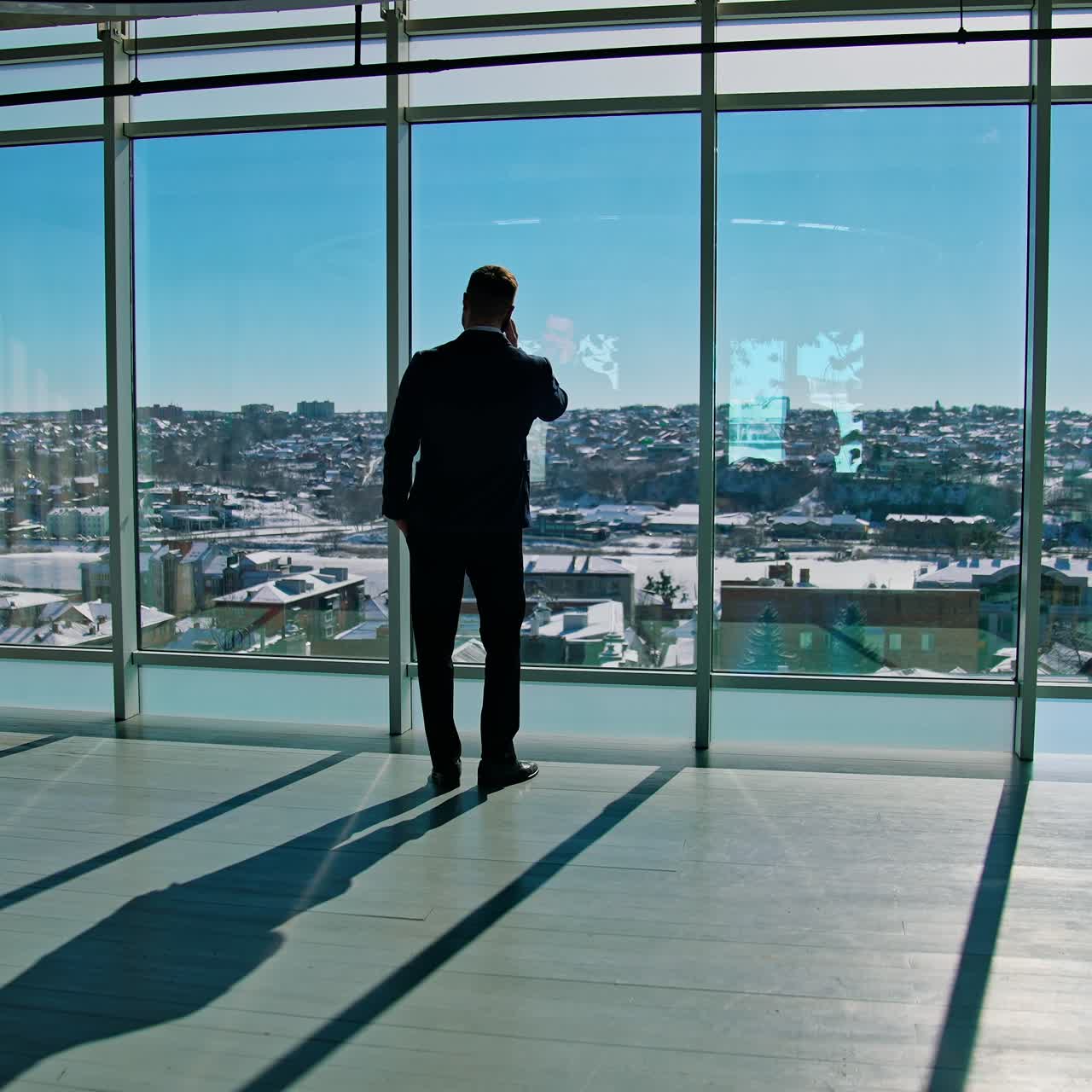 Top manager dealing with business partners through the phone. Male entrepreneur in elegant suit standing by the window and talking the phone. Panoramic windows view