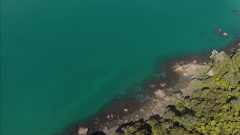 aerial top-down drone moving over green rocky mountains towards a full cyan turquoise lake