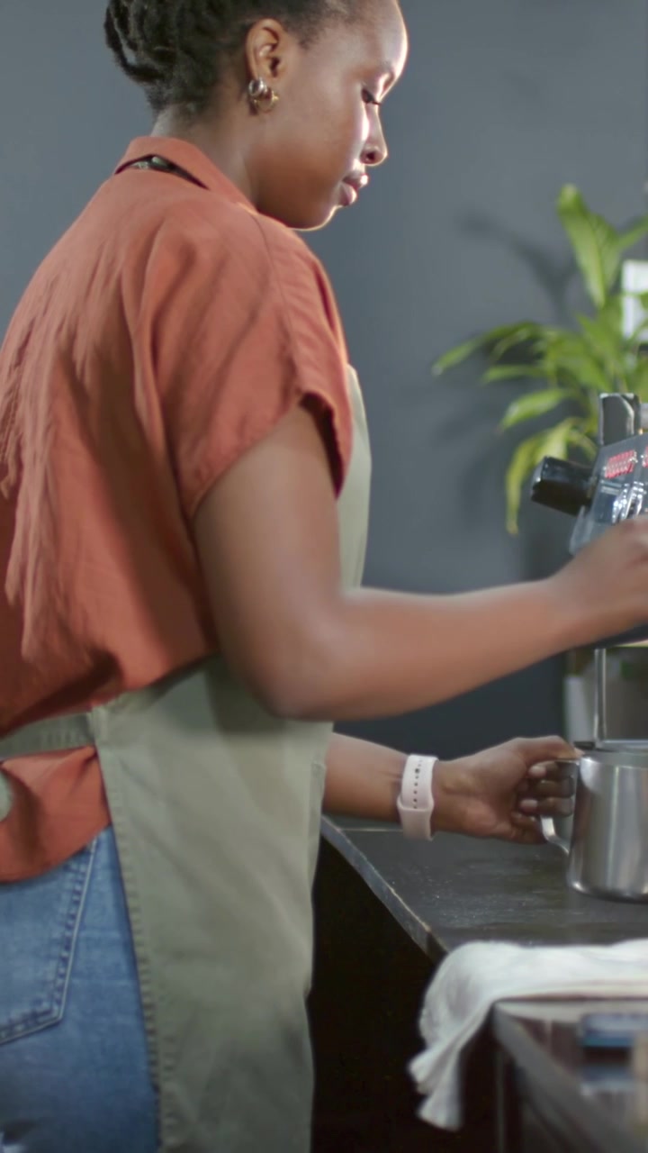 Video verticale: Donna con grembiule che gira una manopola e monta il latte con un bricco alla macchina da caffè espresso per un latte.