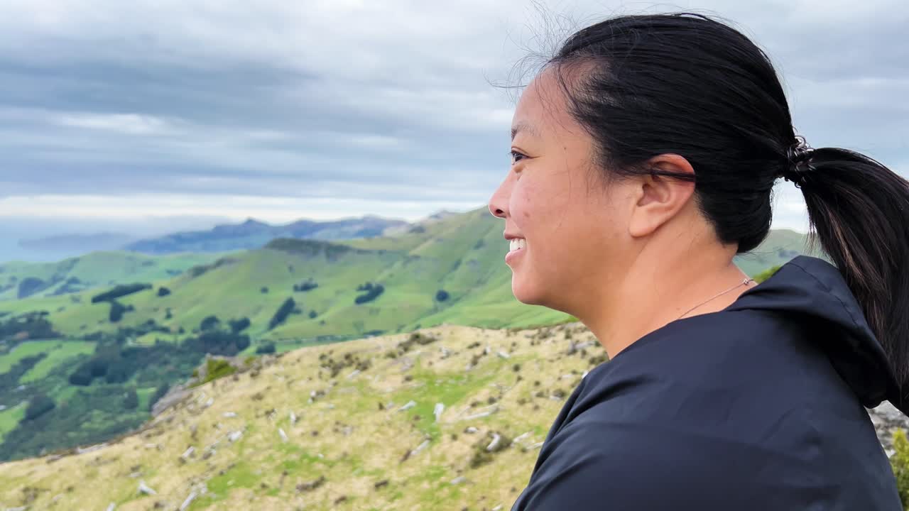 Asian woman smiling on Montgomery Peak, Akaroa Peninsula, embracing nature, close up