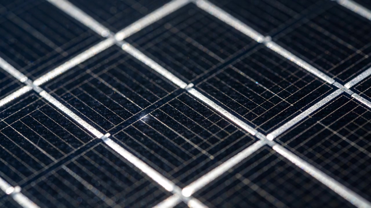 La messa a fuoco della telecamera si sposta rivelando un modulo fotovoltaico su un banco di ispezione, mostrando le sbarre collettrici e una macchia