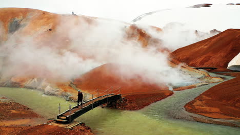 person crossing bridge in kerlingafjoll geothermal area with smoke in highlands of iceland