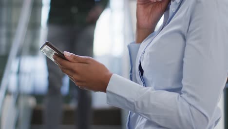 feliz mujer de negocios afroamericana usando un teléfono inteligente en la oficina