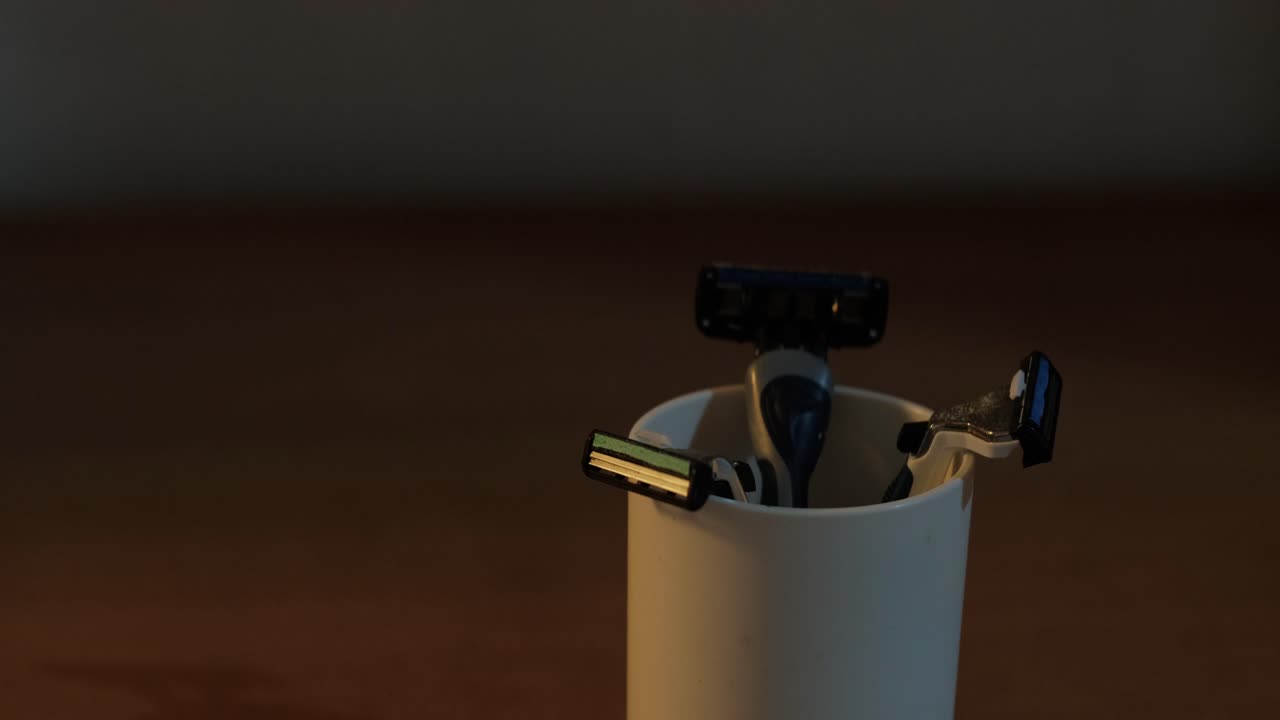 Person Placing A Razor In A Cup Inside The Bathroom. Close-up Shot