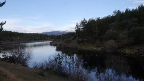 Eine-Langsame-Bewegungsaufnahme-Eines-Ruhigen-Flusses-Und-Einiger-Berge-Im-Hintergrund-Unter-Einem-Blauen-Himmel-Mit-Winzigen-Wolken