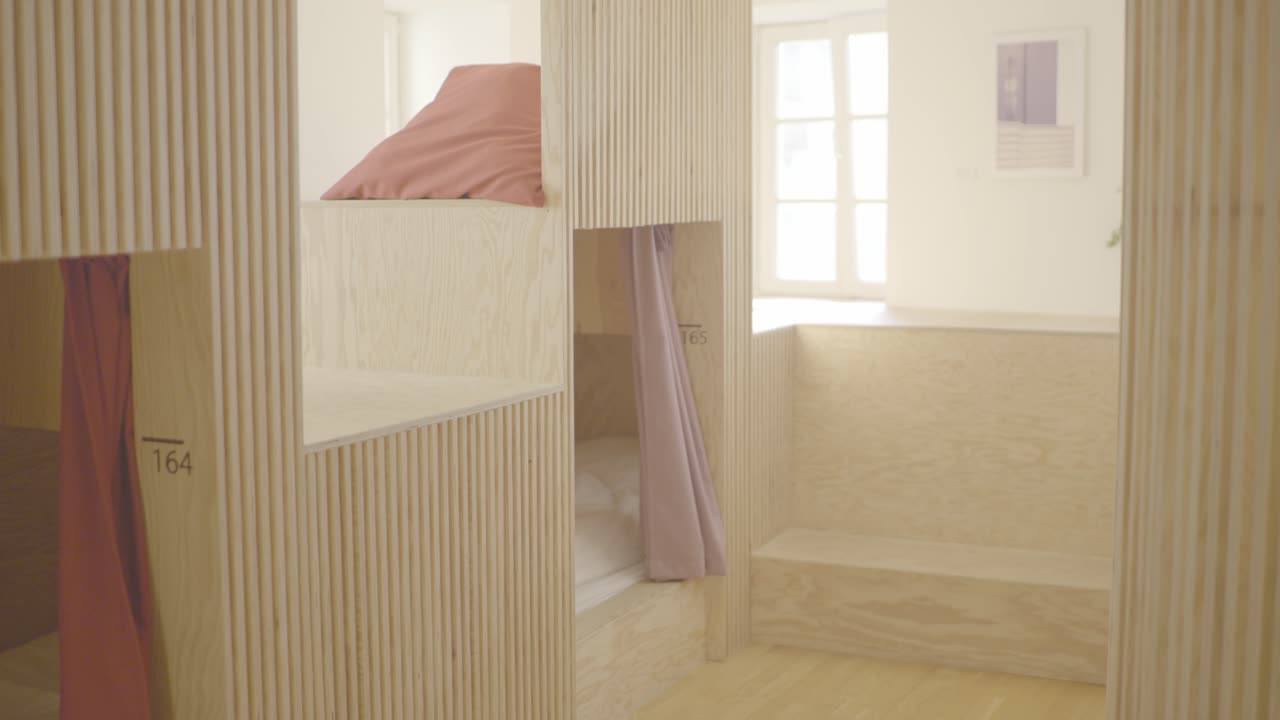 Shot of multiple sleeping cabins in a beautiful wooden modern youth hostel with a warm lamp shining on white sheets