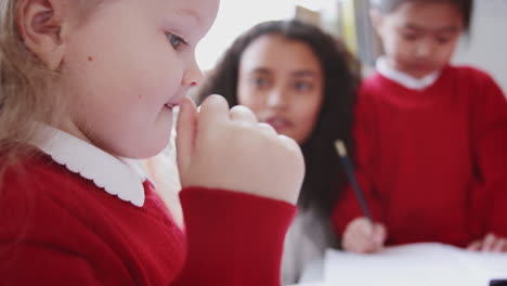 young white schoolgirl drawing at desk in an infant school classroom, close up, side view